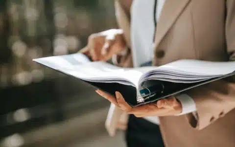 Crop faceless female entrepreneur in formal jacket turning pages of documents in folder while reading